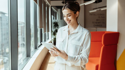 Your Winning Ticket to the Digital Roundtrip of Insurance A woman smiling down at her tablet while standing in front of a wall of windows